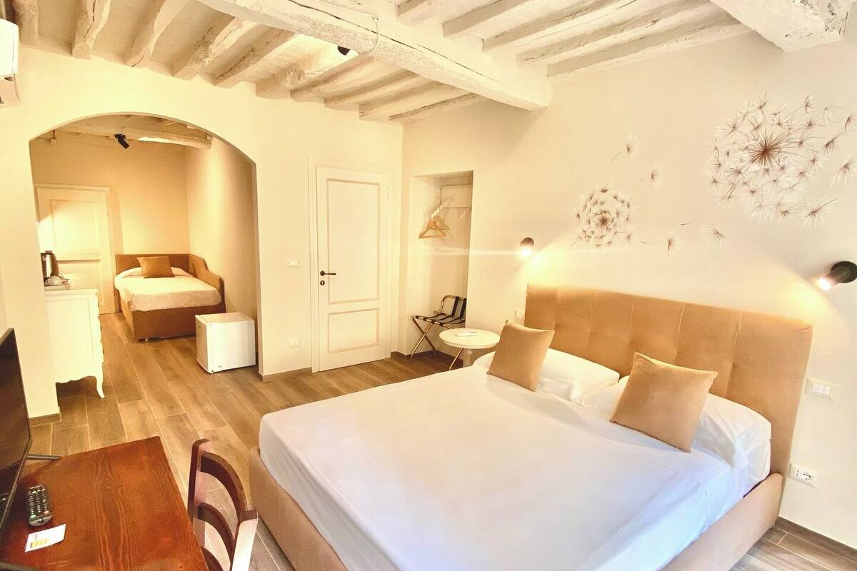 A hotel room with a large bed, a desk, a chair, a small table, and a door leading to another room.