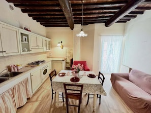 A cozy kitchen with wooden beams, a dining table set for four, and a red sofa in the background.