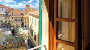 A balcony with a view of a street, a building with a green facade, and a window with a curtain. - CASA AMBRA (Cortona)