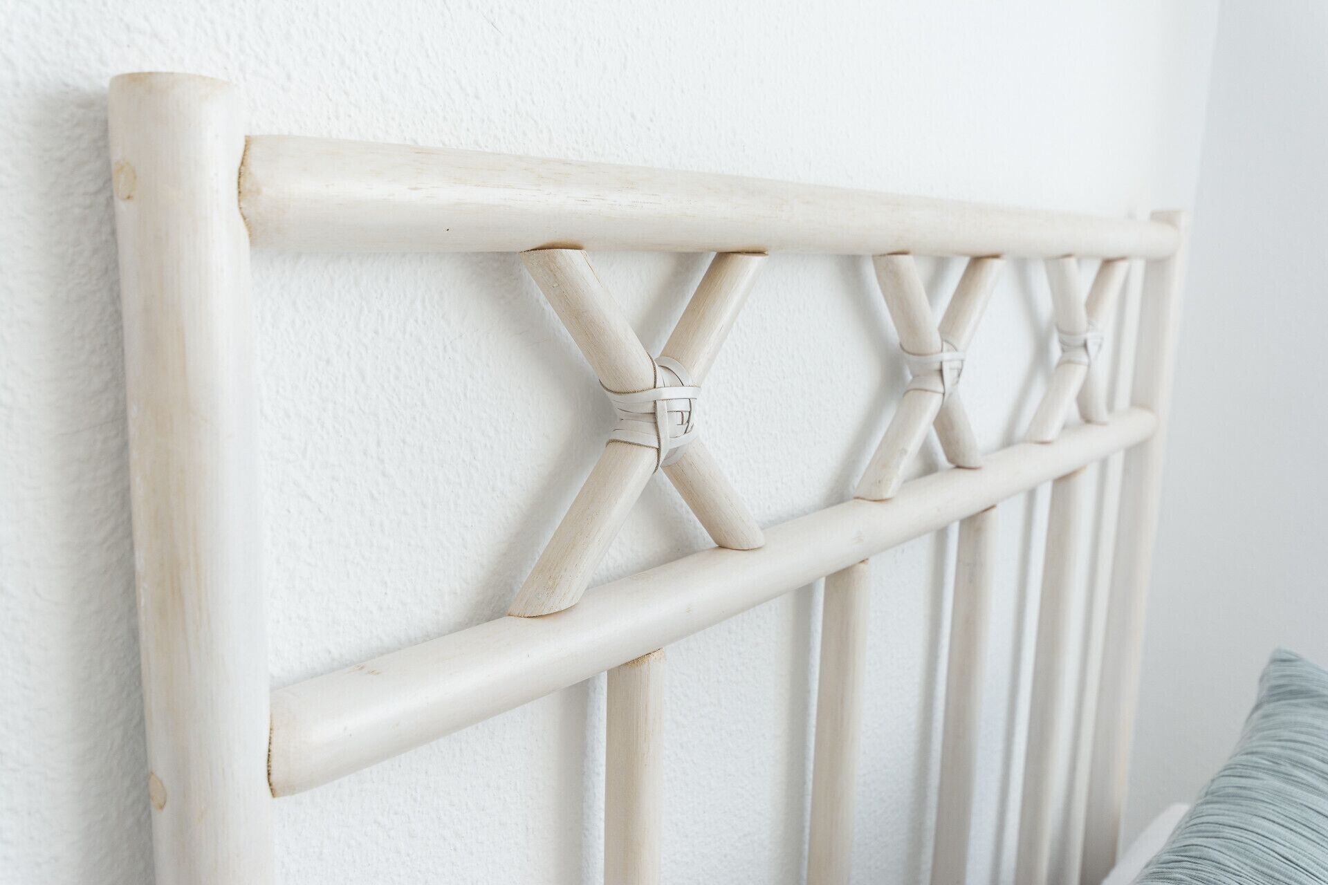 Une tête de lit blanche en bois, ornée d’un motif en croisillons, se dresse devant un mur blanc.