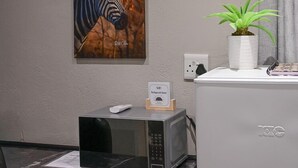 Ett rum med ett skrivbord, en mikrovågsugn, en luftkonditionering, en krukväxt, en tavla med ett zebrabild och en termostat.