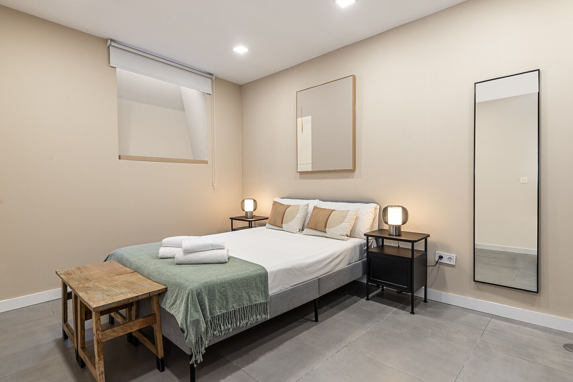 A bedroom with a bed, bedside tables, a bench, and a large mirror.