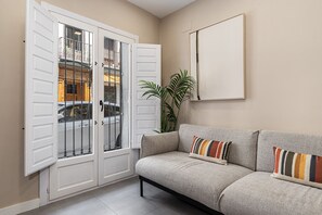 Ein Zimmer mit grauem Sofa, einer weißen Tür mit Glasfeldern und einer Topfpflanze.