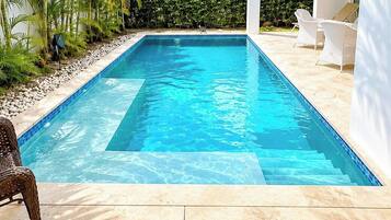 A rectangular swimming pool with clear blue water, surrounded by a light-colored tiled deck.