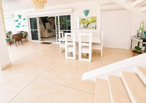 Un vaste espace de vie comprenant un canapé blanc, une table à manger et un escalier menant à un autre niveau.
