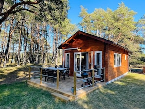 A wooden cabin with a deck, a table, and chairs, surrounded by tall trees. - 4 Person Holiday Home in Yngsjo (Yngsjo)