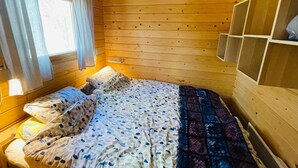 A wooden cabin bedroom with a bed, pillows, a window with curtains, and a shelf unit. - 4 Person Holiday Home in Yngsjo (Yngsjo)