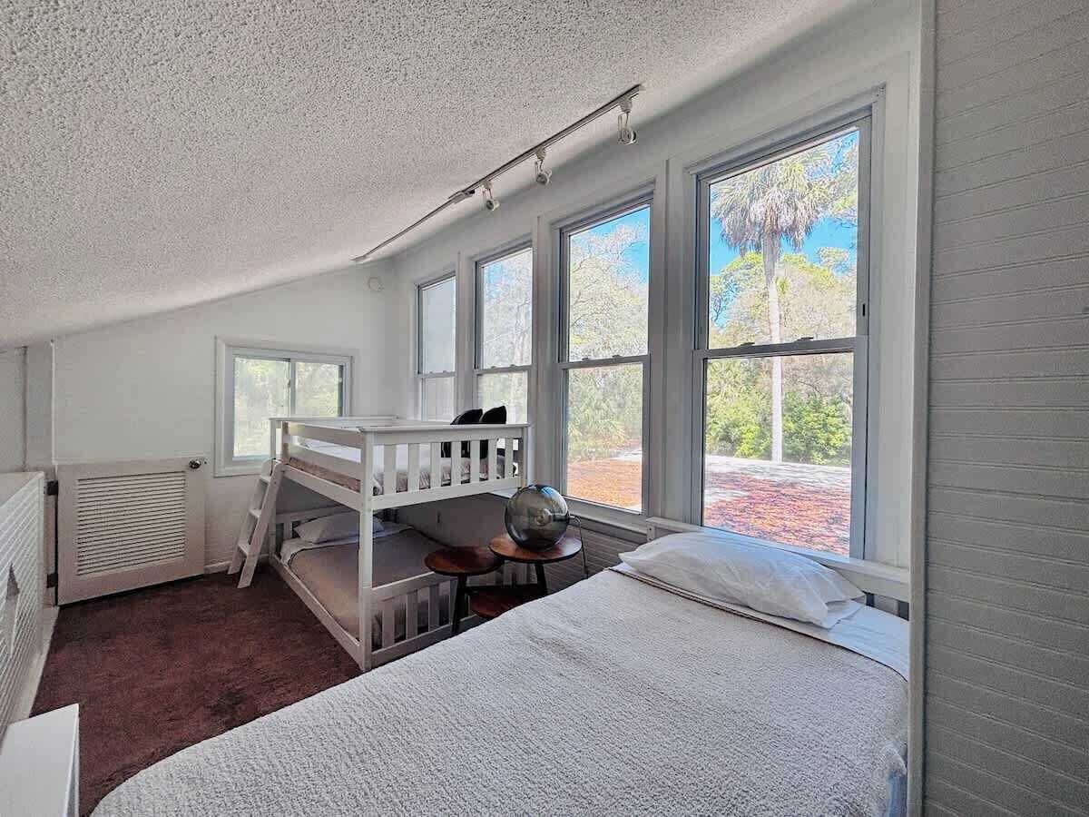 A room with bunk beds, a desk, and large windows.