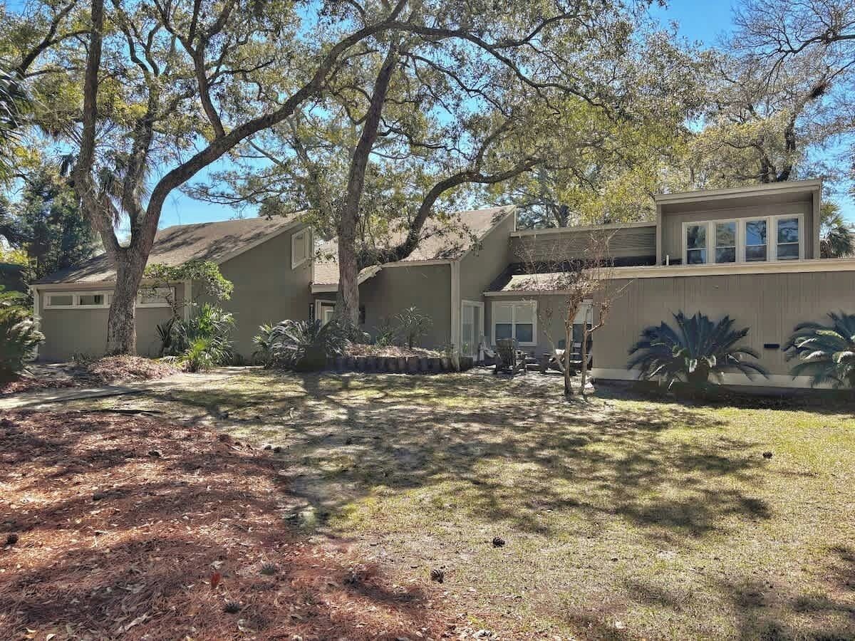 A two-story house with a covered patio, a lawn, and a large tree in the yard.