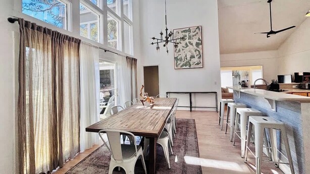 Een ruime keuken met een lange houten tafel, witte barstoelen en een groot raam.