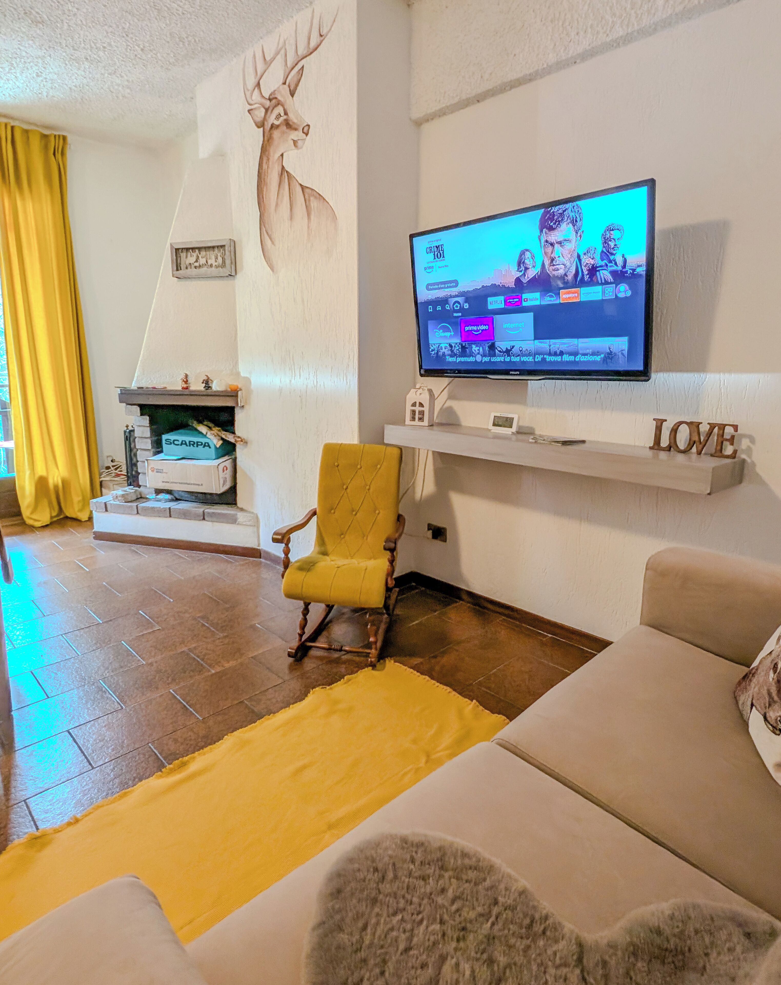 Una sala de estar con televisor, chimenea, un sillón amarillo y un sofá.
