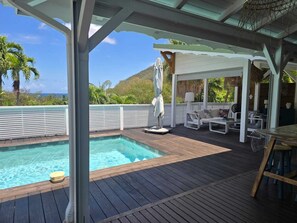 Eine Holzterrasse mit Pool, Liegestühlen und einer überdachten Sitzgruppe mit Meerblick.