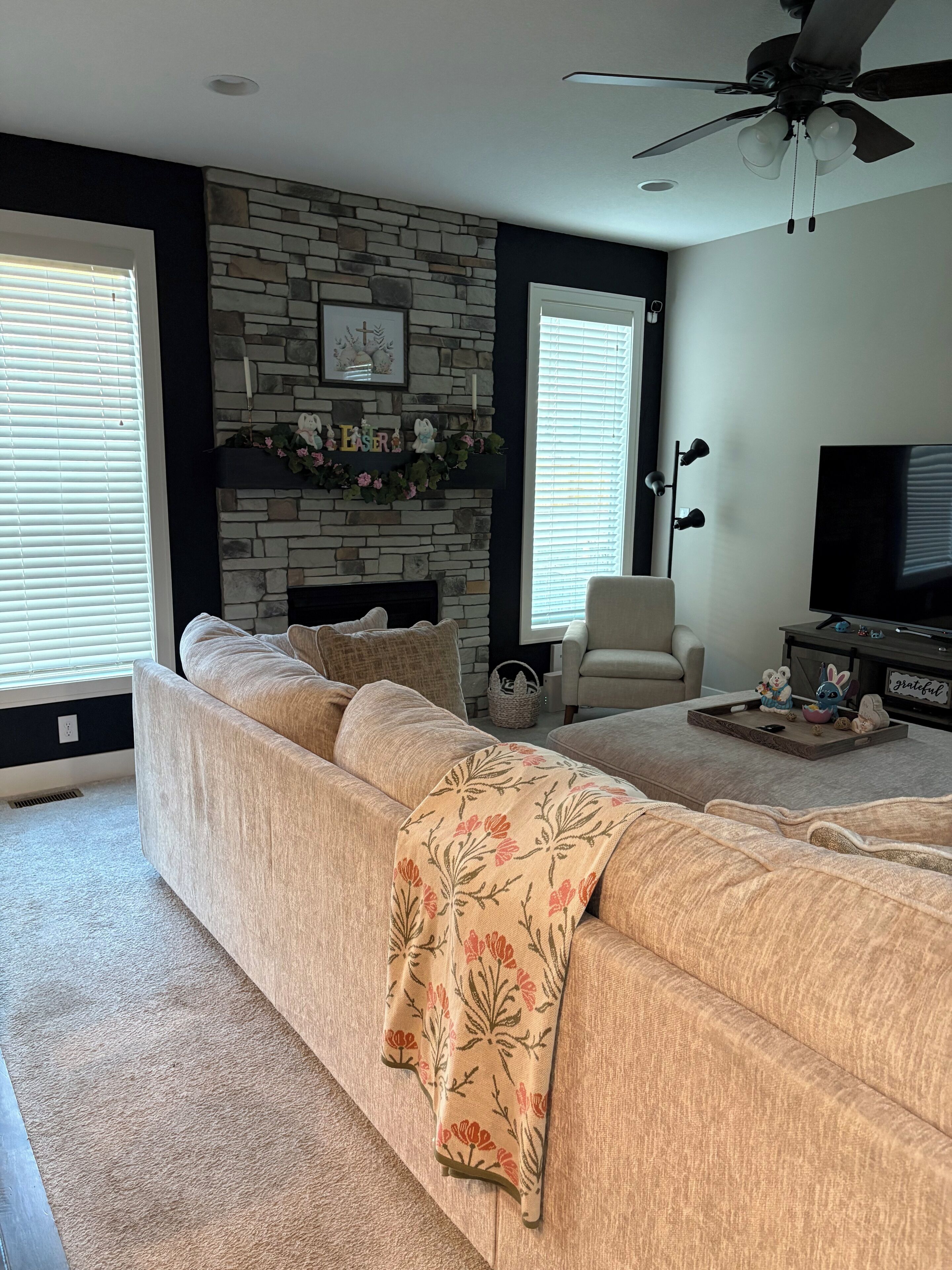 A living room with a stone fireplace, a sofa, a television, and a ceiling fan.