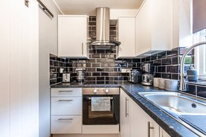 Eine kompakte Küche mit weißen Schränken, einer Edelstahl-Dunstabzugshaube, einem Einbauofen, einer schwarzen Küchenzeile und einem Spülbecken mit einem modernen Wasserhahn.