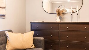 A room with a dark wooden dresser, a mirror, and a single yellow pillow on a gray sofa. - City & Sea: Cosy retreat (Great Yarmouth)
