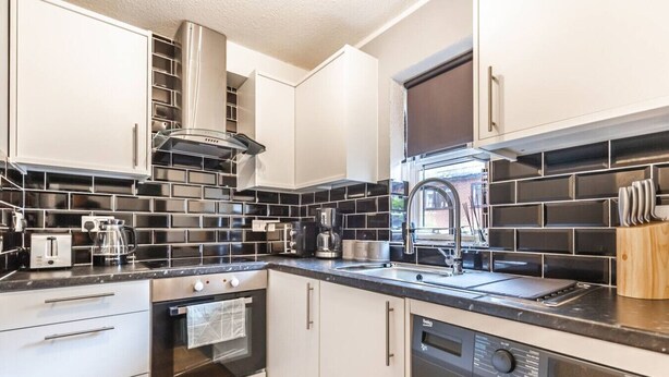 A compact kitchen with white cabinets, black tiled backsplash, stainless steel appliances, and a built-in dishwasher. - City & Sea: Cosy retreat (Great Yarmouth)