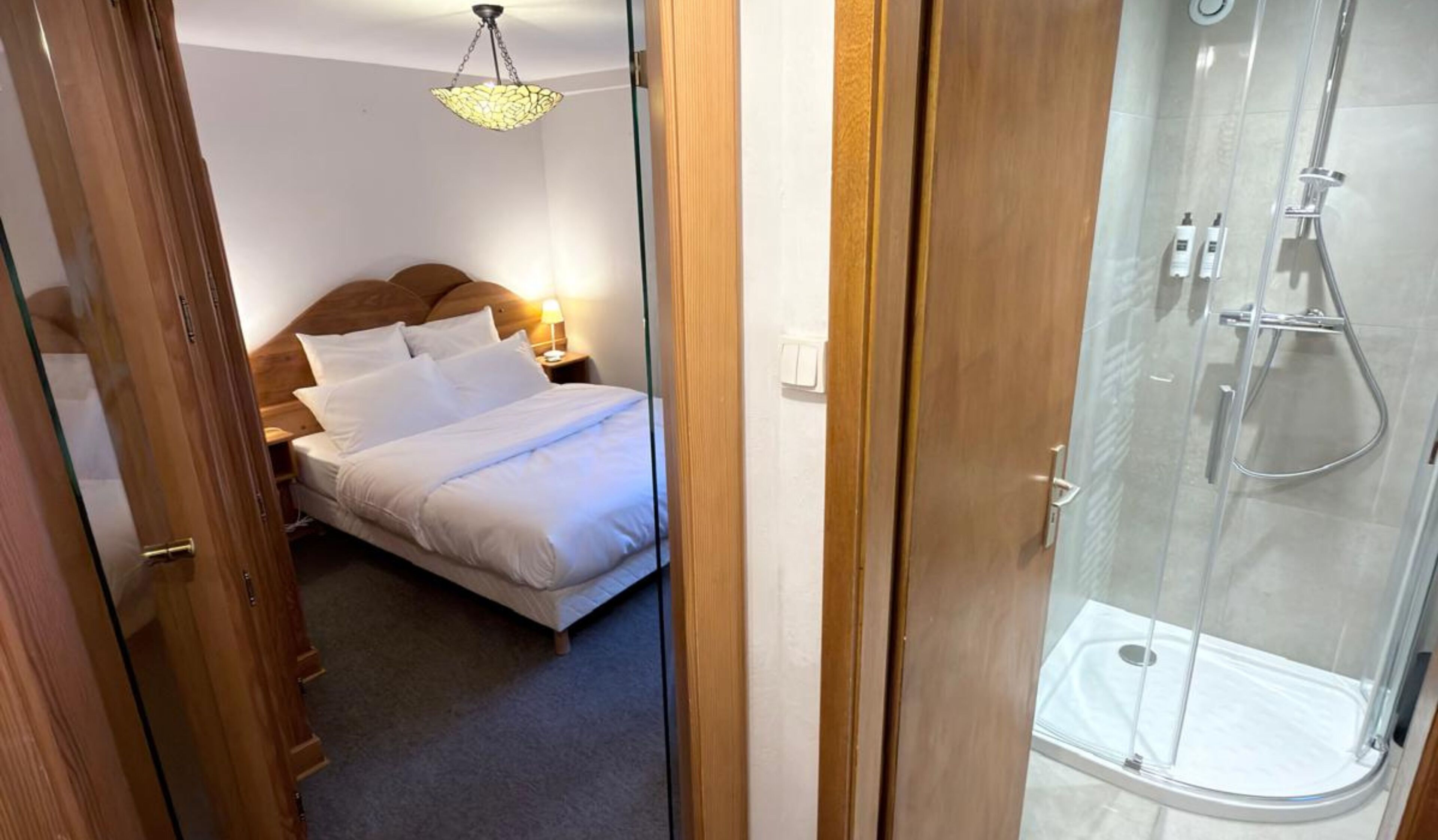 Quarto com cama, mesa de cabeceira e luminária suspensa.