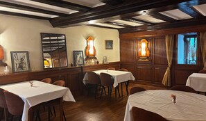 A dining area with wooden paneling, white tablecloths, and framed artwork on the walls.