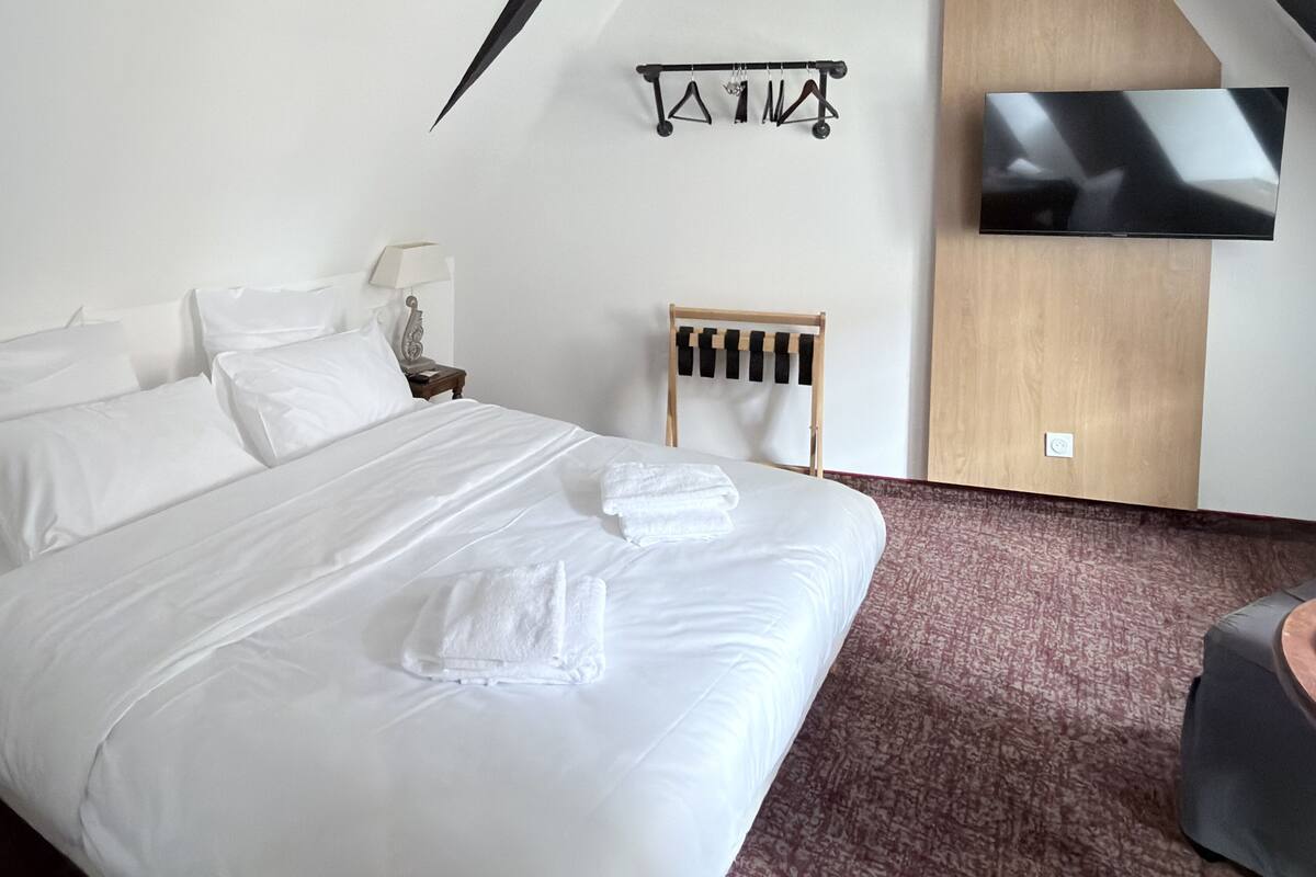 Une chambre d’hôtel avec un lit bien fait, un téléviseur fixé au mur et une petite table d’appoint en bois.