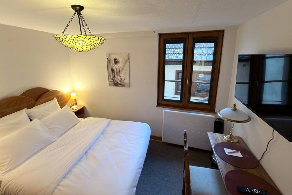 Une chambre d’hôtel avec un lit, une lampe de chevet, une fenêtre et un téléviseur fixé au mur.