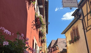 Una calle estrecha con un cartel de hotel, arquitectura tradicional y macetas con flores.