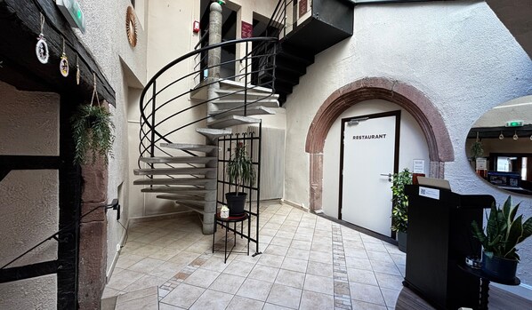 Una escalera de caracol, la puerta de un restaurante y una planta en maceta en el interior de un edificio.