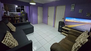 A living room with a sofa, TV, and a kitchen area in the background. - The best modern apartment in Santa Ana with private movie theater and fast internet (Santa Ana)