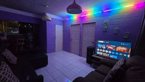 A room with a tiled floor, two doors, a television displaying a streaming service, and a ceiling light fixture. - The best modern apartment in Santa Ana with private movie theater and fast internet (Santa Ana)