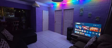 A room with a tiled floor, two doors, a television displaying a streaming service, and a ceiling light fixture.