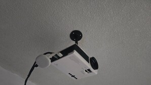 A ceiling-mounted projector with a remote control and a power cord. - The best modern apartment in Santa Ana with private movie theater and fast internet (Santa Ana)