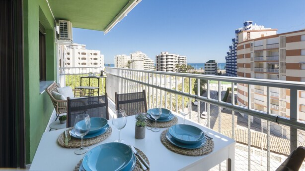 Un balcon avec une table dressée pour le dîner, offrant une vue sur le paysage urbain et la mer.