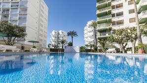 Une piscine à l’eau d’un bleu cristallin, entourée de bâtiments modernes dotés de balcons et de palmiers.