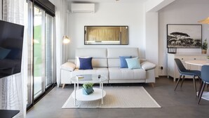 Un salon moderne comprenant un canapé, une table basse, un ventilateur de plafond et un coin repas avec des chaises.