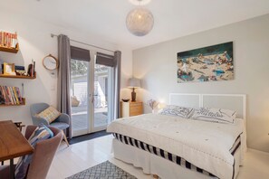 A bedroom with a bed, a desk, a chair, a bookshelf, a painting, and a sliding glass door leading to an outdoor area.