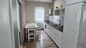 Una cucina moderna con mobili bianchi, pavimento in legno e una finestra con persiane.