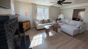 A living room with a fireplace, two sofas, a coffee table, a ceiling fan, and a window with curtains. - 6BR Sleep 20 DT Amarillo Tech/Data Ctr Corp Stays (Amarillo)