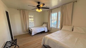 A bedroom with a bed, a chair, a ceiling fan, and two windows with curtains. - 6BR Sleep 20 DT Amarillo Tech/Data Ctr Corp Stays (Amarillo)