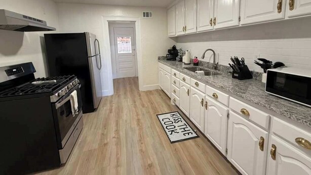 A kitchen with white cabinets, a black stove, a refrigerator, and a microwave. - 6BR Sleep 20 DT Amarillo Tech/Data Ctr Corp Stays (Amarillo)