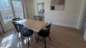 A dining area with a wooden table and black chairs, large windows with curtains, and a kitchen in the background. - 6BR Sleep 20 DT Amarillo Tech/Data Ctr Corp Stays (Amarillo)