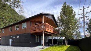 A two-story house with a balcony, a gravel driveway, and a grassy yard. - Relax comfortably & enjoy a 2-bedroom studio in Valdez perfect for your getaway. (Valdez)