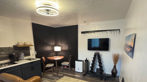 A modern living room with a sofa, a dining area, a kitchen, and a TV mounted on the wall. - Relax comfortably & enjoy a 2-bedroom studio in Valdez perfect for your getaway. (Valdez)