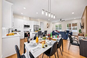 A modern kitchen with white cabinets, a dining area with a table set for breakfast, and a living area with a sofa and a TV. - Private Patio | Ground Floor | Near Busch Gardens (Tampa)