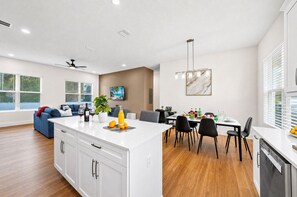 Une cuisine moderne avec des meubles blancs, un îlot central et un coin repas comprenant une table et des chaises.