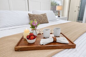A neatly made bed with white linens, a wooden tray with a candle, strawberries, a mug, and a small vase with flowers. - Private Patio | Ground Floor | Near Busch Gardens (Tampa)