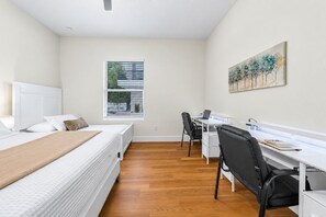 A bedroom with a bed, a desk, and a chair. There is a window with blinds, a painting on the wall, and a radiator under the bed. - Private Patio | Ground Floor | Near Busch Gardens (Tampa)