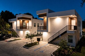 Un moderno edificio residencial de varios pisos con un área de estacionamiento y un pequeño árbol.