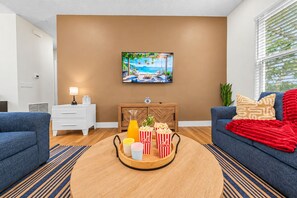 Un salon avec une table basse en bois, deux canapés, un téléviseur et un tableau accroché au mur.