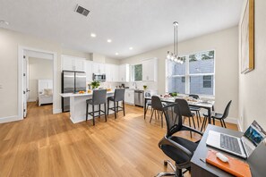 Une cuisine moderne avec des meubles blancs, un îlot central doté de tabourets et un coin repas avec une table et des chaises.