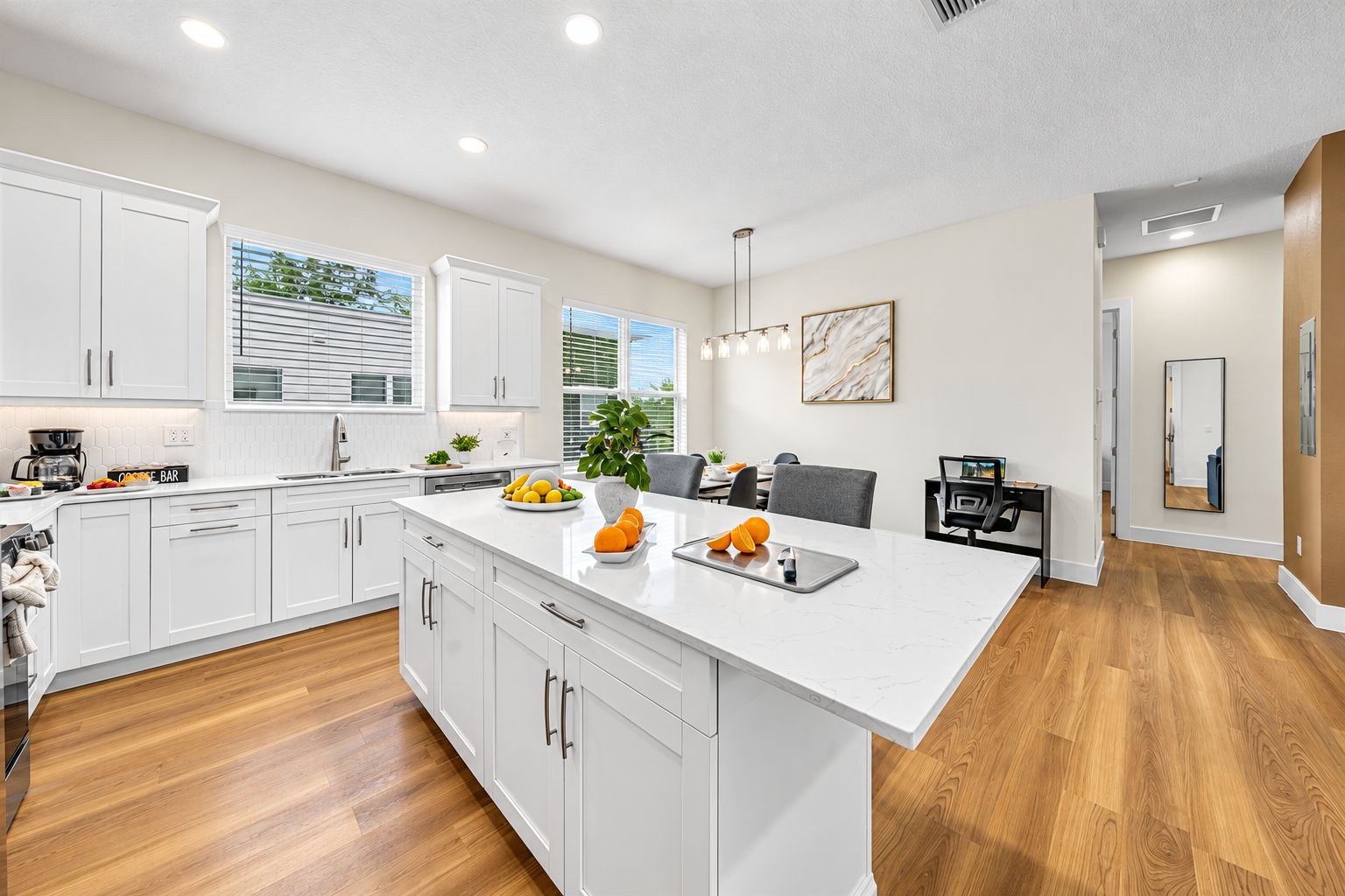A modern kitchen with white cabinetry, a central island, and a dining area with a gray chair.