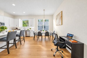 Una cocina moderna con armarios blancos, un comedor con mesa y sillas, y un espacio de trabajo con escritorio y silla.